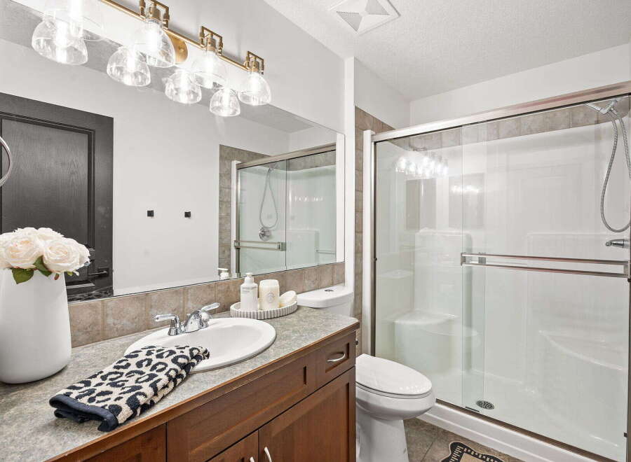 This bathroom features a spacious vanity with a large mirror and elegant lighting, complemented by a modern glass-enclosed shower.