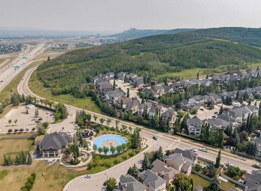 Discover this stunning aerial view of a suburban neighborhood featuring a mix of modern and traditional homes, nestled beside a lush green hillside and a winding highway.