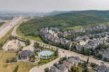 Discover this stunning aerial view of a suburban neighborhood featuring a mix of modern and traditional homes, nestled beside a lush green hillside and a winding highway.