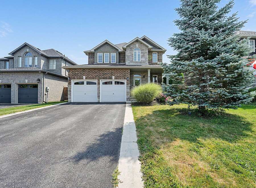 This stunning two-story home boasts a classic brick and stone facade, complemented by a well-maintained lawn and mature evergreen tree.