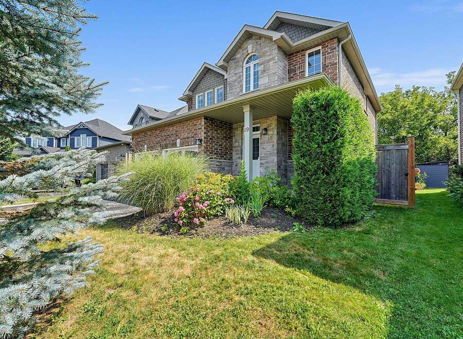 This charming two-story home features a beautiful stone and brick facade, complemented by lush landscaping and a welcoming covered porch.