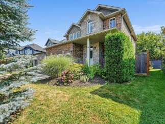 This charming two-story home features a beautiful stone and brick facade, complemented by lush landscaping and a welcoming covered porch.