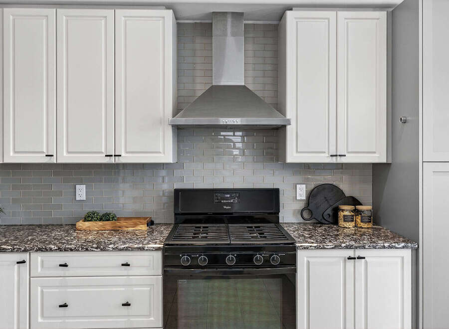 This modern kitchen features sleek white cabinetry and a stylish grey subway tile backsplash.