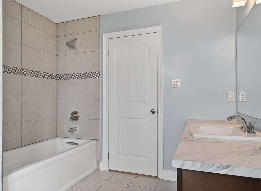 This bathroom features a clean and modern aesthetic with a white bathtub and shower combination, accented by stylish tiled walls.