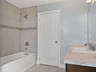 This bathroom features a clean and modern aesthetic with a white bathtub and shower combination, accented by stylish tiled walls.