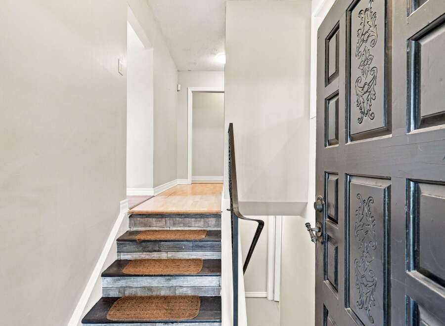 Step into this welcoming entryway featuring a beautifully decorated staircase with textured treads and a dark, ornate door.