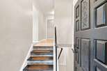 Step into this welcoming entryway featuring a beautifully decorated staircase with textured treads and a dark, ornate door.