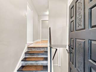Step into this welcoming entryway featuring a beautifully decorated staircase with textured treads and a dark, ornate door.
