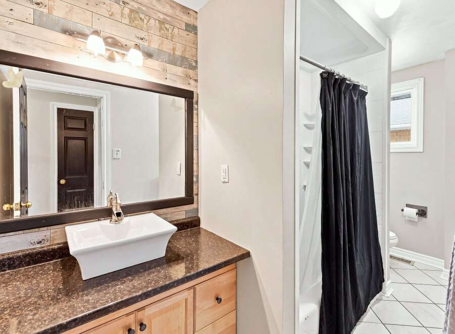 This bathroom features a stylish vessel sink atop a dark speckled countertop and light wood vanity.