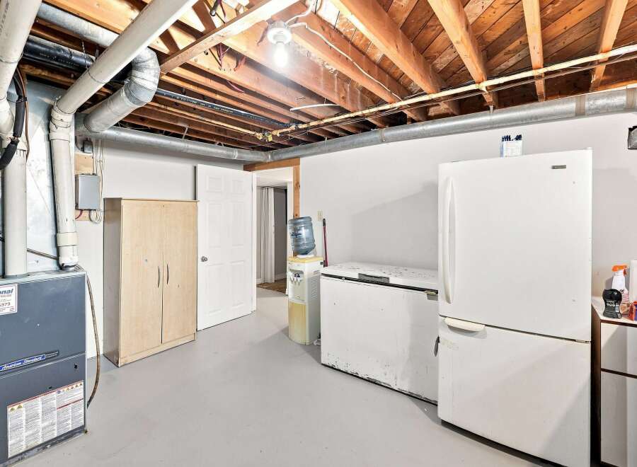 Discover the potential of this basement space, featuring a functional furnace and ample storage with a tall wooden cabinet.