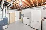 Discover the potential of this basement space, featuring a functional furnace and ample storage with a tall wooden cabinet.