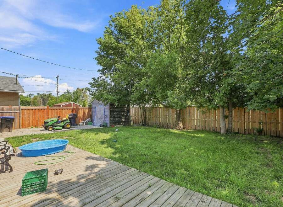 Enjoy outdoor living in this spacious backyard featuring a wooden deck, a blue kiddie pool, and a well-maintained lawn perfect for recreation.