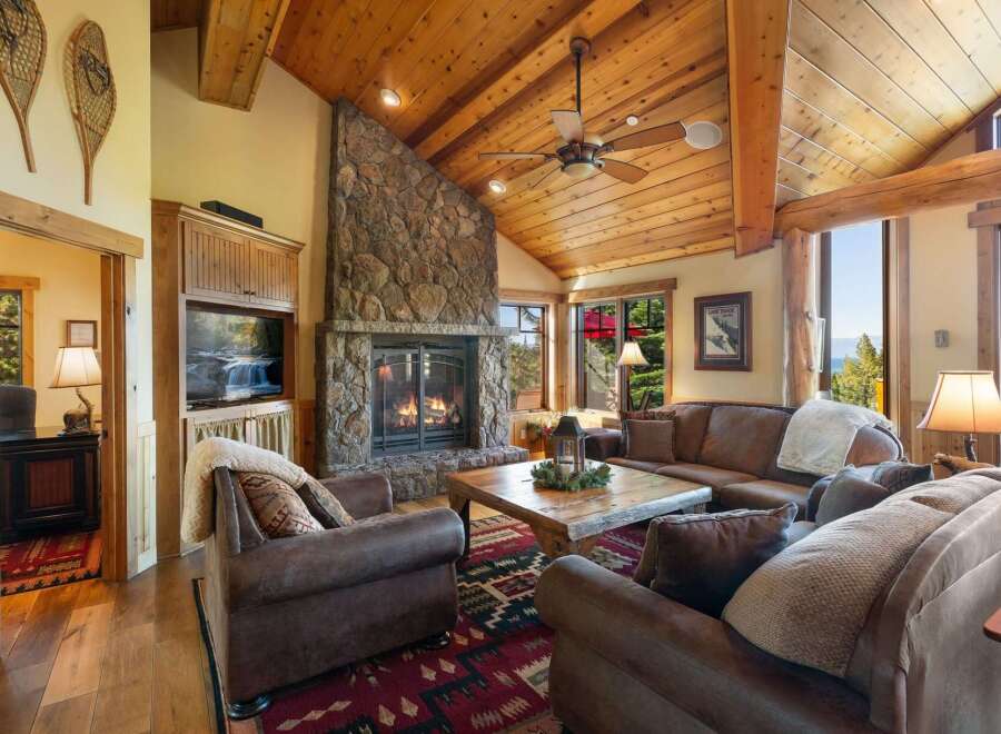 Experience rustic elegance in this stunning living room, featuring a grand stone fireplace and a vaulted wood-paneled ceiling.