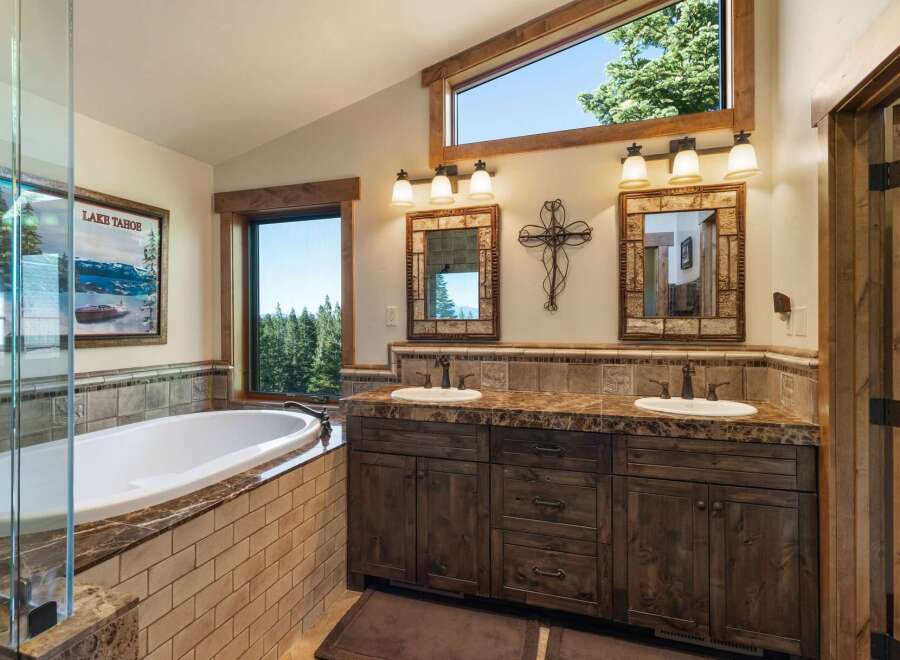 Indulge in luxury in this stunning bathroom featuring a deep soaking tub with a view of the serene lake and surrounding forest.