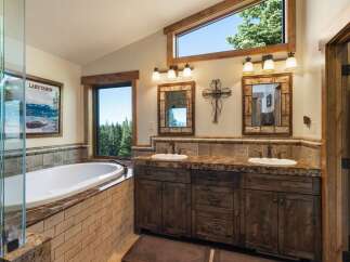 Indulge in luxury in this stunning bathroom featuring a deep soaking tub with a view of the serene lake and surrounding forest.