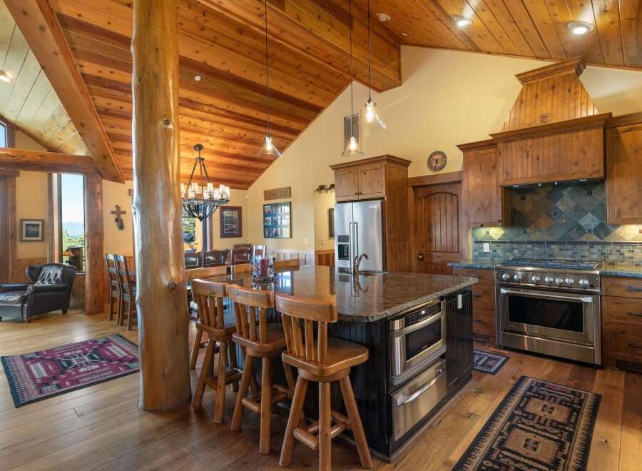 Experience rustic luxury in this stunning log cabin kitchen, featuring a grand wooden beam structure and a spacious island with granite countertops.