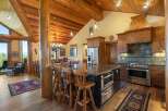 Experience rustic luxury in this stunning log cabin kitchen, featuring a grand wooden beam structure and a spacious island with granite countertops.