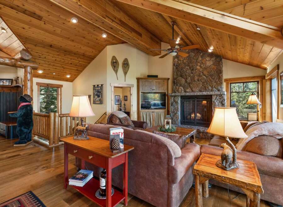 Experience rustic charm in this inviting living room, featuring a grand stone fireplace and a vaulted wood-paneled ceiling.