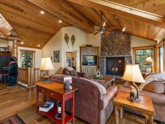 Experience rustic charm in this inviting living room, featuring a grand stone fireplace and a vaulted wood-paneled ceiling.