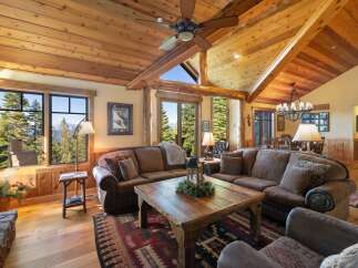 Experience rustic luxury in this stunning mountain lodge living room, featuring a grand stone fireplace and soaring vaulted ceilings with exposed wooden beams.