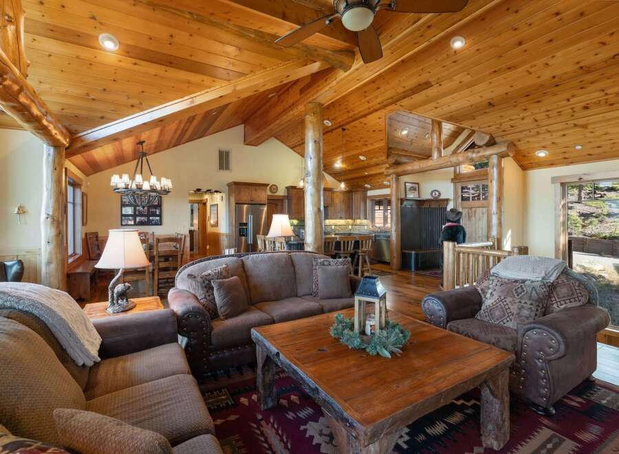 Experience rustic charm in this spacious living area, featuring a vaulted wood-paneled ceiling with exposed beams and a cozy stone fireplace.