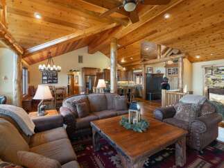 Experience rustic charm in this spacious living area, featuring a vaulted wood-paneled ceiling with exposed beams and a cozy stone fireplace.