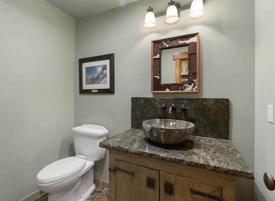 This rustic bathroom features a unique stone vessel sink atop a distressed wood vanity, complemented by a cowhide-framed mirror.
