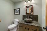 This rustic bathroom features a unique stone vessel sink atop a distressed wood vanity, complemented by a cowhide-framed mirror.