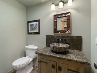 This rustic bathroom features a unique stone vessel sink atop a distressed wood vanity, complemented by a cowhide-framed mirror.