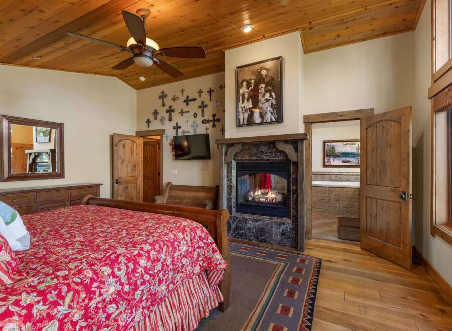 Experience rustic charm in this master bedroom featuring a cozy fireplace and a luxurious soaking tub visible through an open doorway.