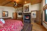 Experience rustic charm in this master bedroom featuring a cozy fireplace and a luxurious soaking tub visible through an open doorway.