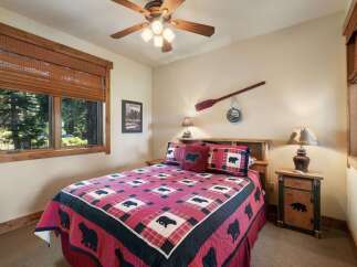 Experience rustic charm in this cozy bedroom, featuring a queen-sized bed adorned with a charming bear-themed quilt and matching pillows.
