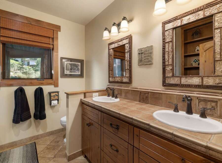This rustic bathroom features a double vanity with warm wood cabinetry and tiled countertops, complemented by oil-rubbed bronze fixtures.