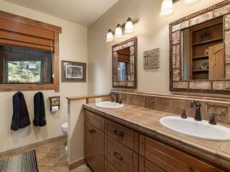 This rustic bathroom features a double vanity with warm wood cabinetry and tiled countertops, complemented by oil-rubbed bronze fixtures.