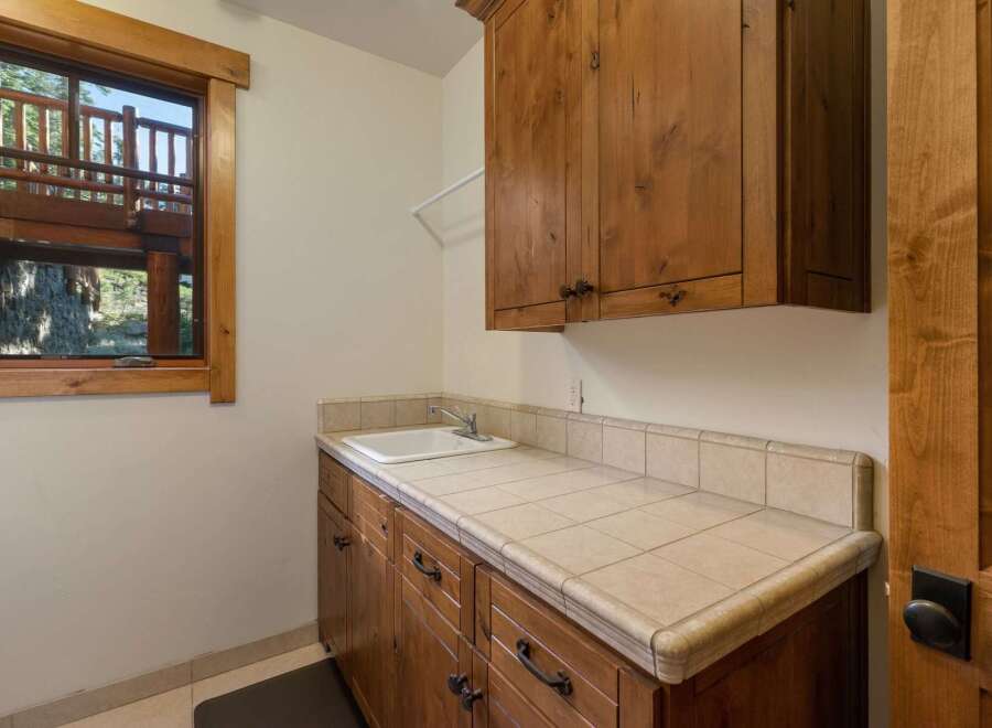 This laundry room features a large wooden vanity with a tiled countertop and a deep sink, perfect for household chores.