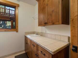 This laundry room features a large wooden vanity with a tiled countertop and a deep sink, perfect for household chores.