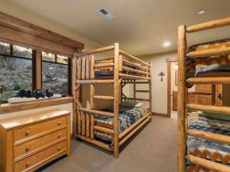 Experience rustic charm in this bedroom featuring a triple bunk bed crafted from natural logs, perfect for accommodating guests or family.