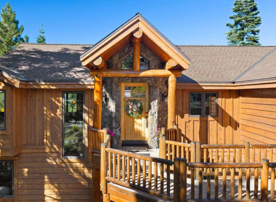Experience rustic charm in this mountain retreat featuring a beautiful log-accented entrance with a stone facade and a welcoming wooden door adorned with a wreath.