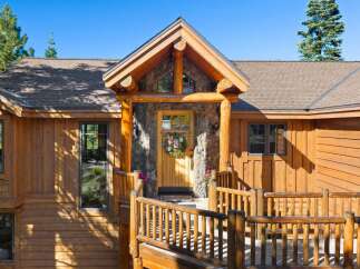 Experience rustic charm in this mountain retreat featuring a beautiful log-accented entrance with a stone facade and a welcoming wooden door adorned with a wreath.