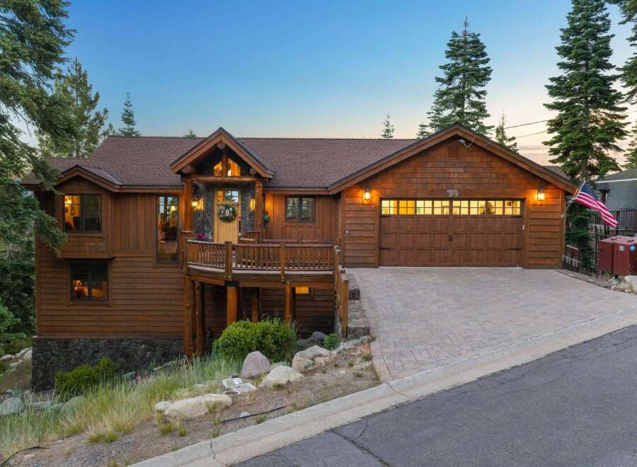 Experience rustic charm in this stunning wood-sided home, featuring a welcoming covered porch with a wooden deck and stone accents.