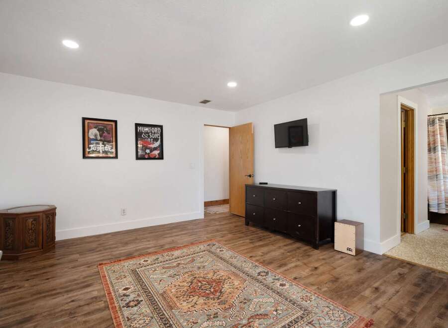 This spacious room features a large area rug, a dark wood dresser, and a wall-mounted television, perfect for entertainment.