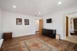 This spacious room features a large area rug, a dark wood dresser, and a wall-mounted television, perfect for entertainment.
