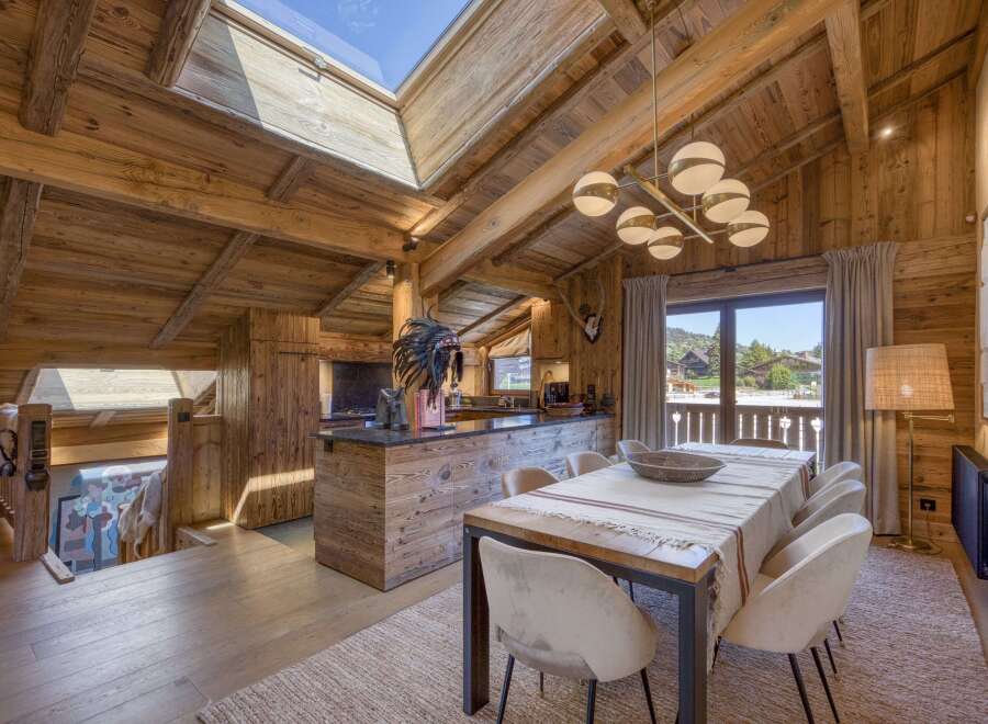 Experience luxurious alpine living in this stunning wooden chalet, featuring a spacious open-plan dining and kitchen area with a large island and modern chandelier.