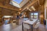 Experience luxurious alpine living in this stunning wooden chalet, featuring a spacious open-plan dining and kitchen area with a large island and modern chandelier.