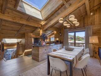 Experience luxurious alpine living in this stunning wooden chalet, featuring a spacious open-plan dining and kitchen area with a large island and modern chandelier.