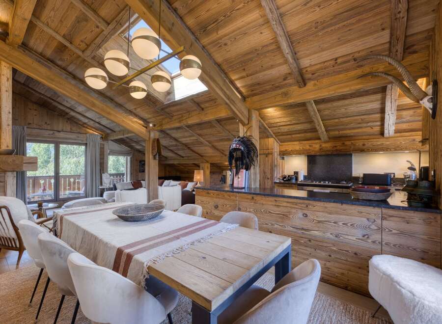 Experience rustic luxury in this stunning alpine dining and kitchen area, featuring a grand wooden-beamed ceiling and a large dining table perfect for gatherings.