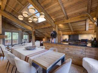 Experience rustic luxury in this stunning alpine dining and kitchen area, featuring a grand wooden-beamed ceiling and a large dining table perfect for gatherings.
