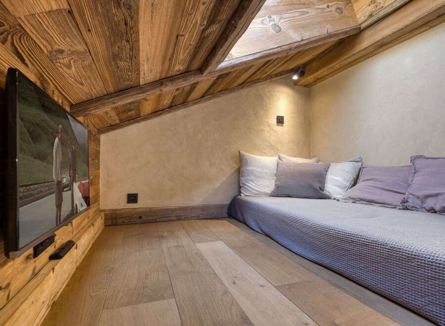 Experience cozy living in this charming attic room, featuring rustic wooden walls and ceiling, complemented by a comfortable daybed with plush pillows.