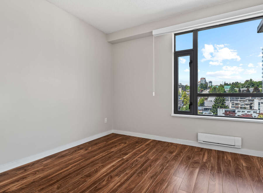 Experience modern living in this spacious room featuring elegant hardwood floors and a large window with stunning city views.