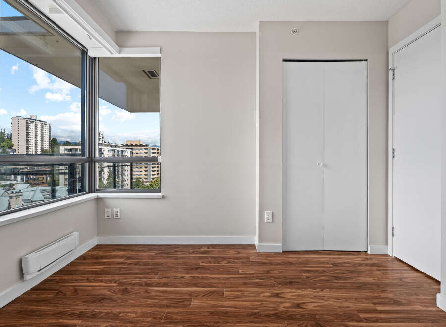 Experience modern living in this spacious room featuring a large window with city views and rich hardwood flooring.